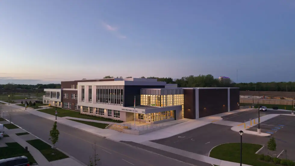Exterior view of White Pine Public School at dusk, showcasing its modern architecture, well-lit entrance, and adjacent parking lot.