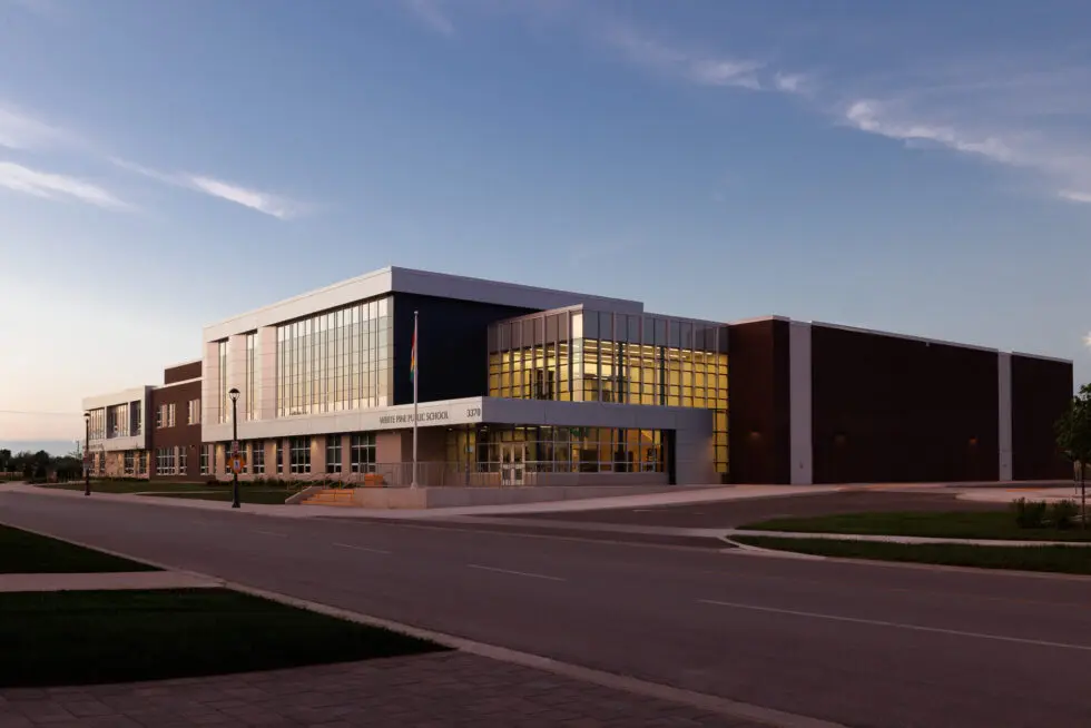 Exterior view of White Pine Public School at dusk, showcasing its modern architecture, glass facade, and dark brick sections under a clear sky.