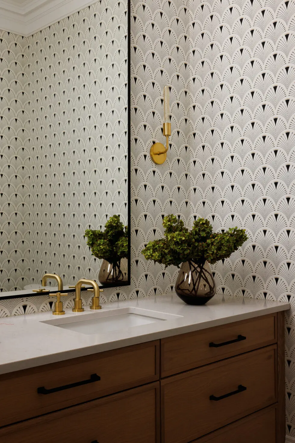 Art Deco fan pattern wallpaper in a stylish powder room with a white marble vanity, gold faucet, wooden cabinet, and green plant.