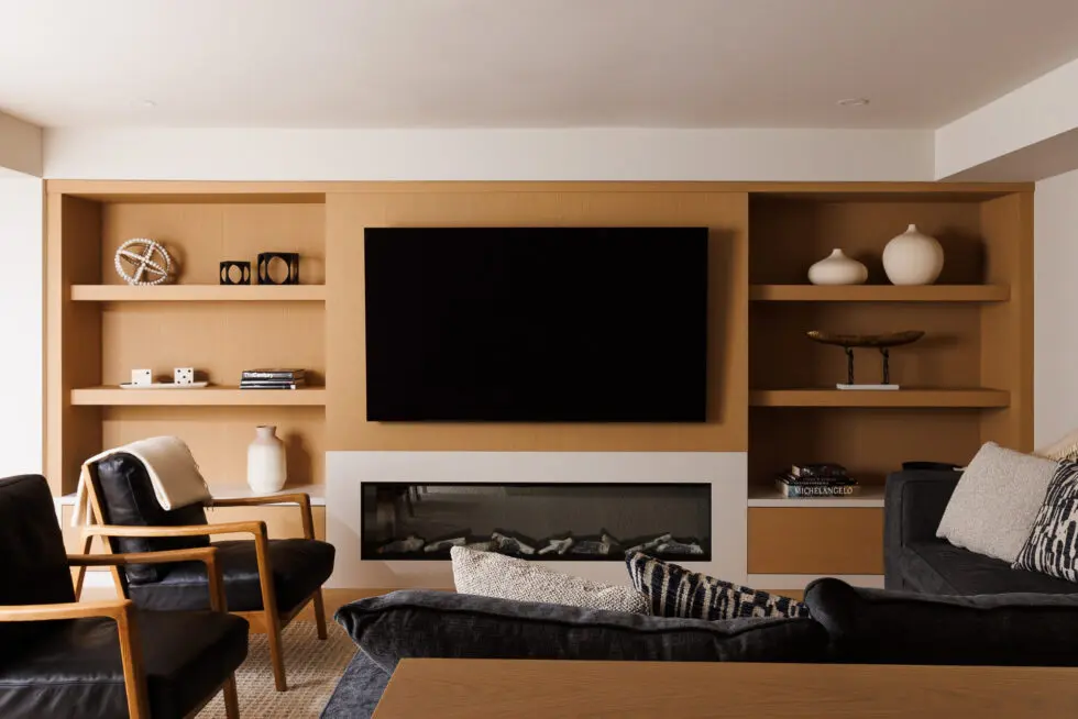 Modern living room with custom light wood built-in media center, featuring a large TV, linear fireplace, and decorative shelving.