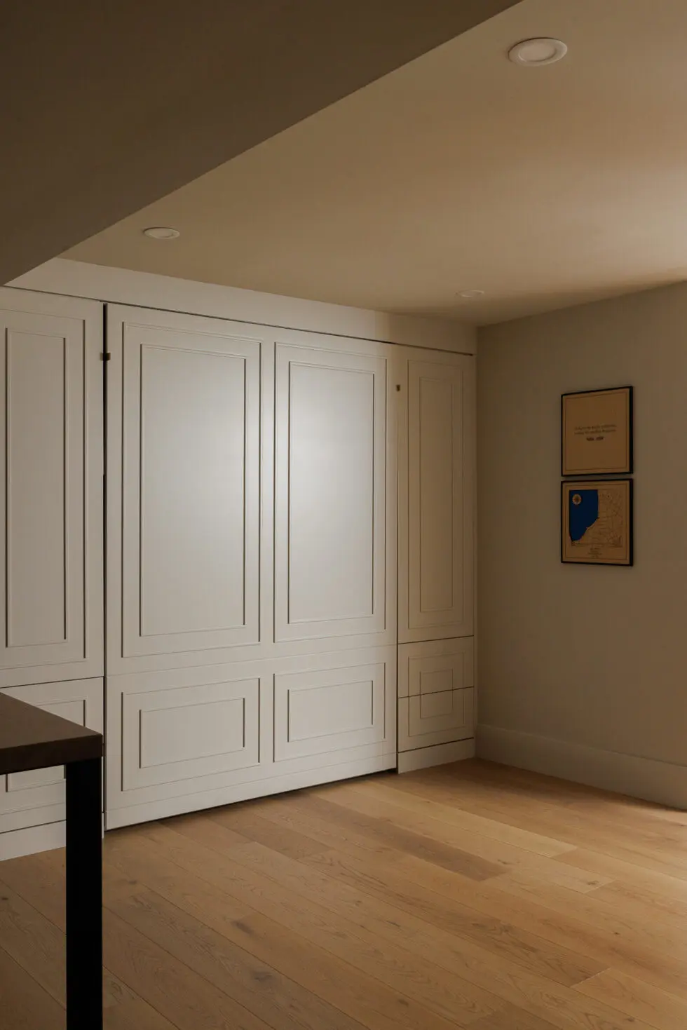 Modern built-in wall bed or custom cabinet system in a neutral room with light wood flooring and recessed lighting