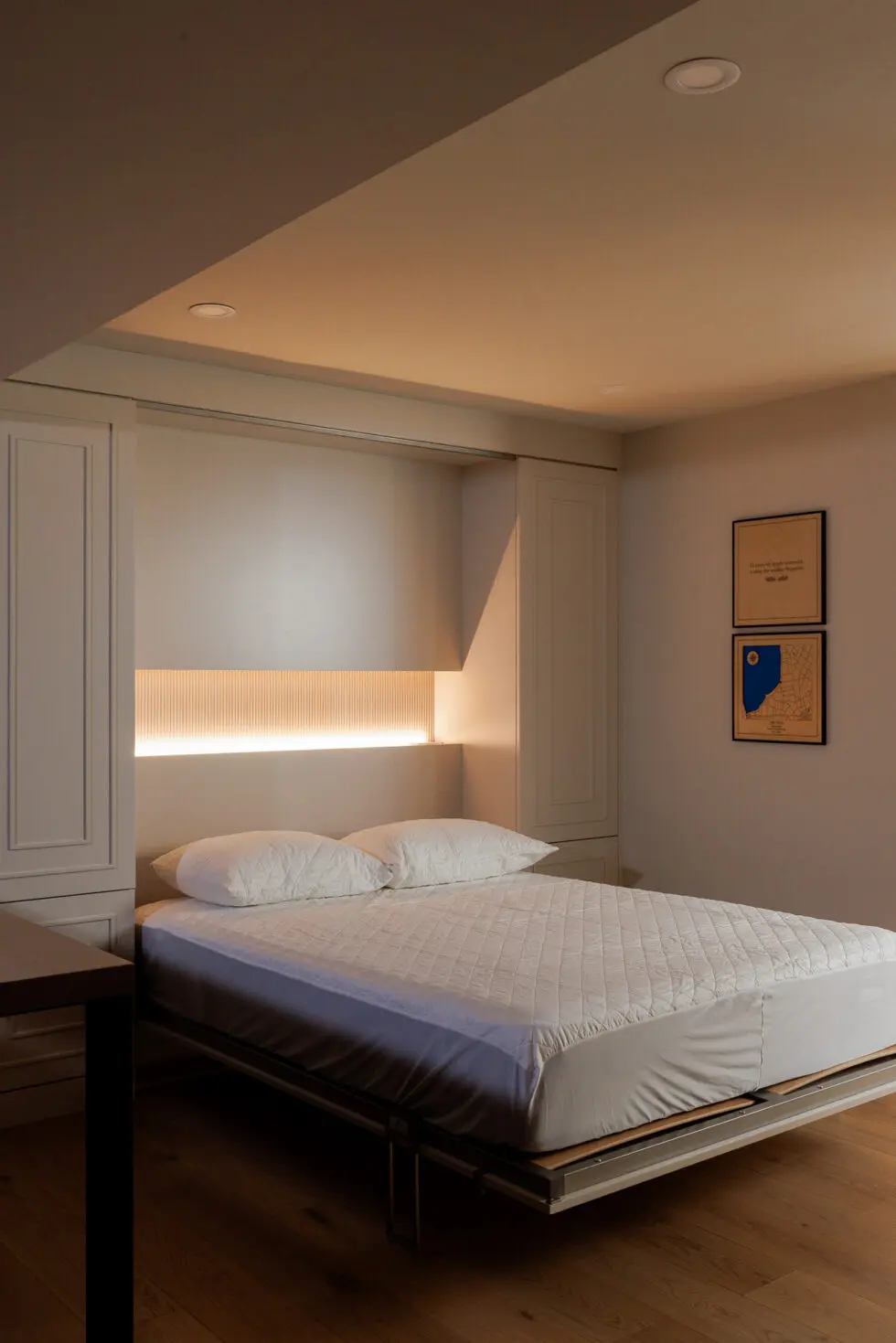Modern bedroom with a bed, white bedding, built-in fluted headboard with warm LED lighting, and wood floor.