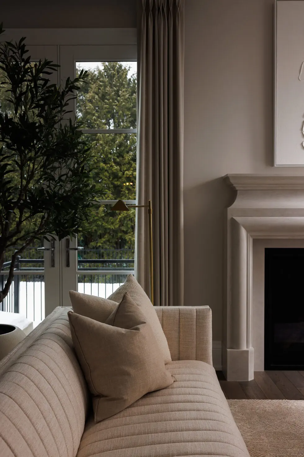 Elegant neutral living room with textured beige sofa, stone fireplace, and large windows overlooking a snowy treeline