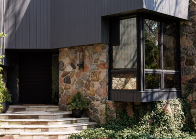 Modern house exterior with dark gray siding, natural stone facade, bay window, and ivy landscaping