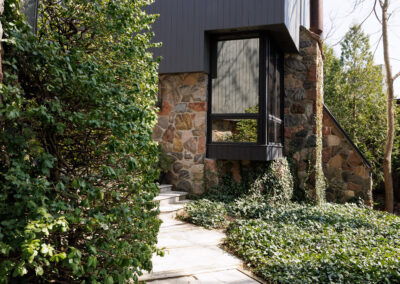 Modern house entrance with stone path, dark grey siding, and lush green landscaping