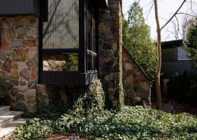 Modern home exterior with dark grey siding, natural stone facade, and lush ivy ground cover