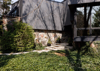 Modern house exterior with dark grey vertical siding, natural stone foundation, lush green ivy ground cover, and stone steps.