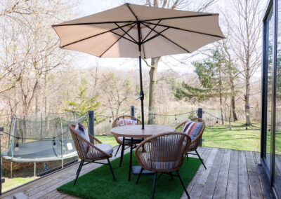Outdoor patio deck with wicker dining set, beige umbrella, and scenic river view with a trampoline.