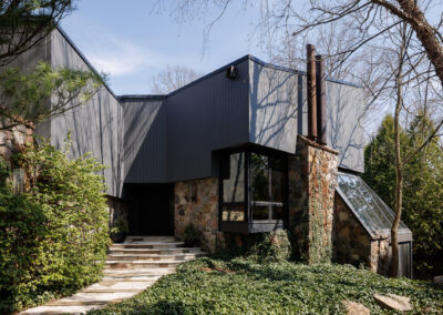 Modern house exterior with dark grey siding and natural stone facade amidst lush green landscaping
