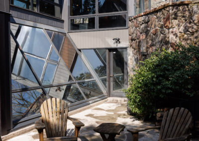 Modern home exterior with angular glass windows, stone wall, flagstone patio, Adirondack chairs, and fire pit