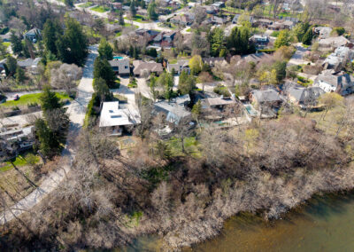 Aerial view of a suburban residential neighborhood with houses, winding roads, mature trees, and a river winding along the property lines during early spring.