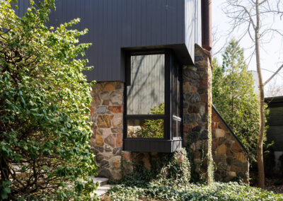 Modern house exterior with dark gray siding, natural stone facade, and a lush green garden pathway