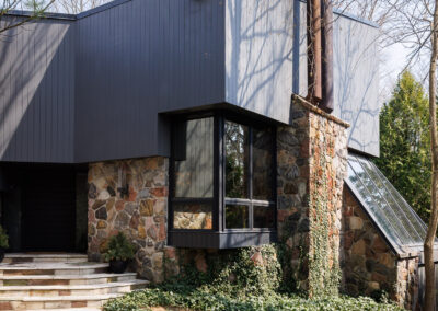 Modern house exterior with dark gray siding and stone facade, featuring a bay window and ivy-covered walls