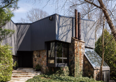 Modern dark gray house with stone facade, prominent chimney, glass skylight, and lush ivy landscaping.