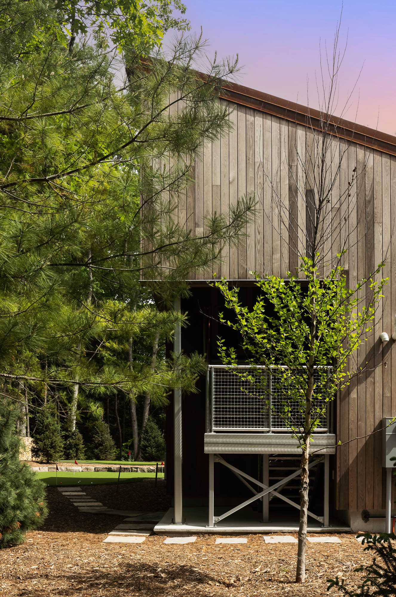 Industrial Exterior Detail and Landscaping Vertical close-up of a modern metal balcony and staircase against wood cladding, with a putting green in the background.