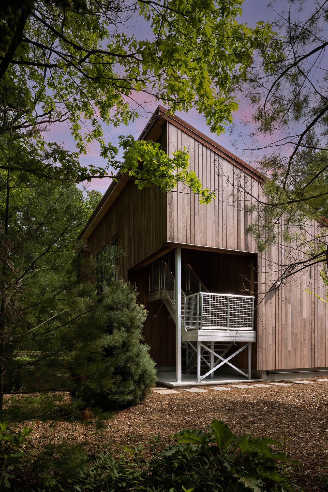 Architectural Detail of Custom Wood Garage Exterior Close-up of vertical cedar siding and a galvanized steel staircase on a modern garage, framed by lush green trees.
