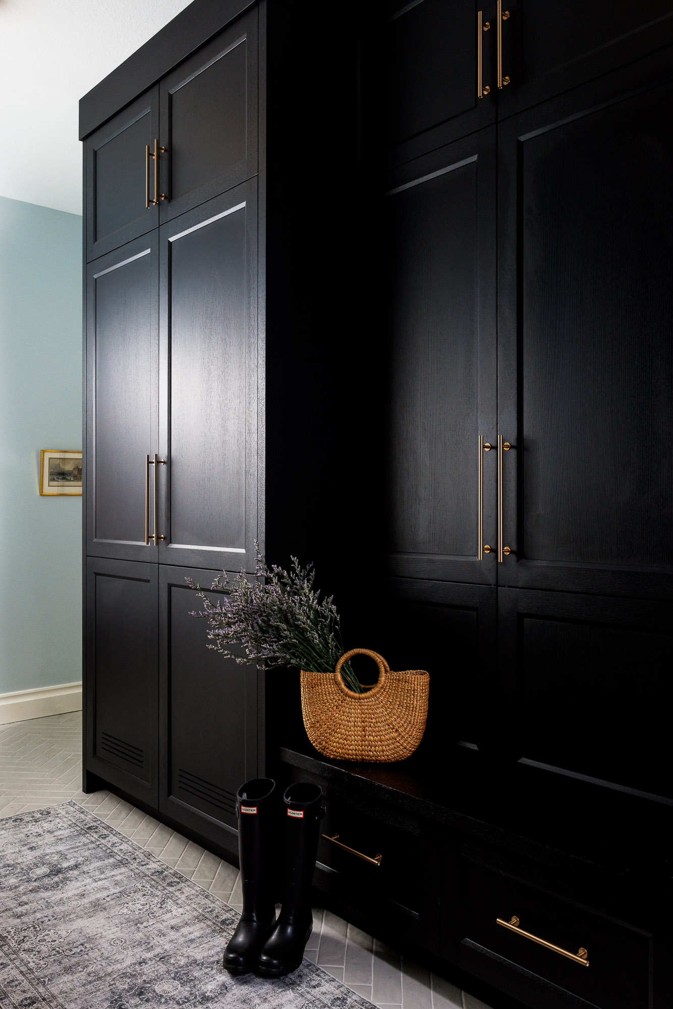Sophisticated Entryway with Custom Matte Black Cabinetry Architectural shot of a mudroom featuring floor-to-ceiling matte black cabinetry with vertical brass handles, a built-in bench, and black rain boots.