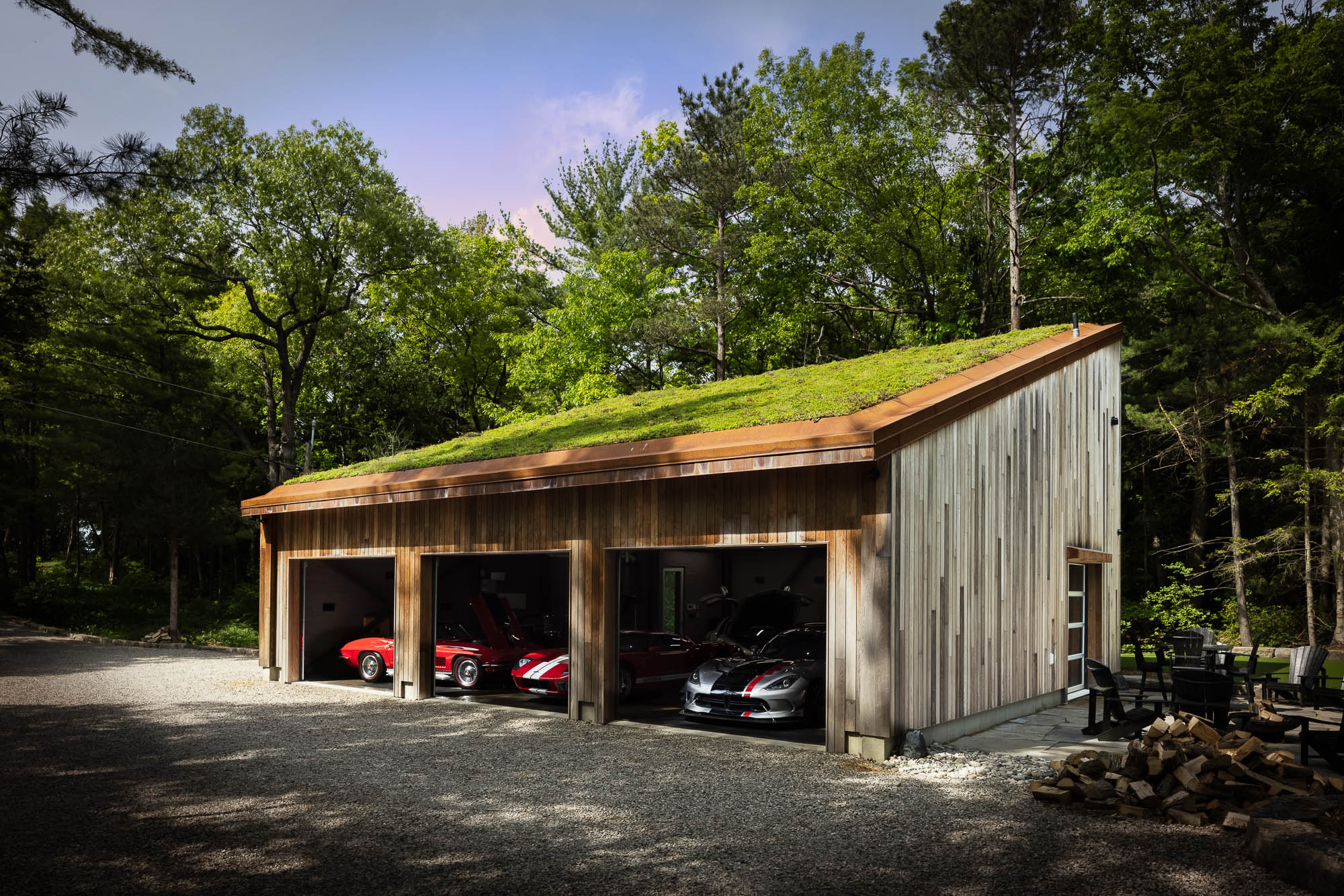 Luxury Garage with Sustainable Living Roof Wide exterior view of a three-bay modern wood garage featuring a lush green roof and housing a collection of sports cars.