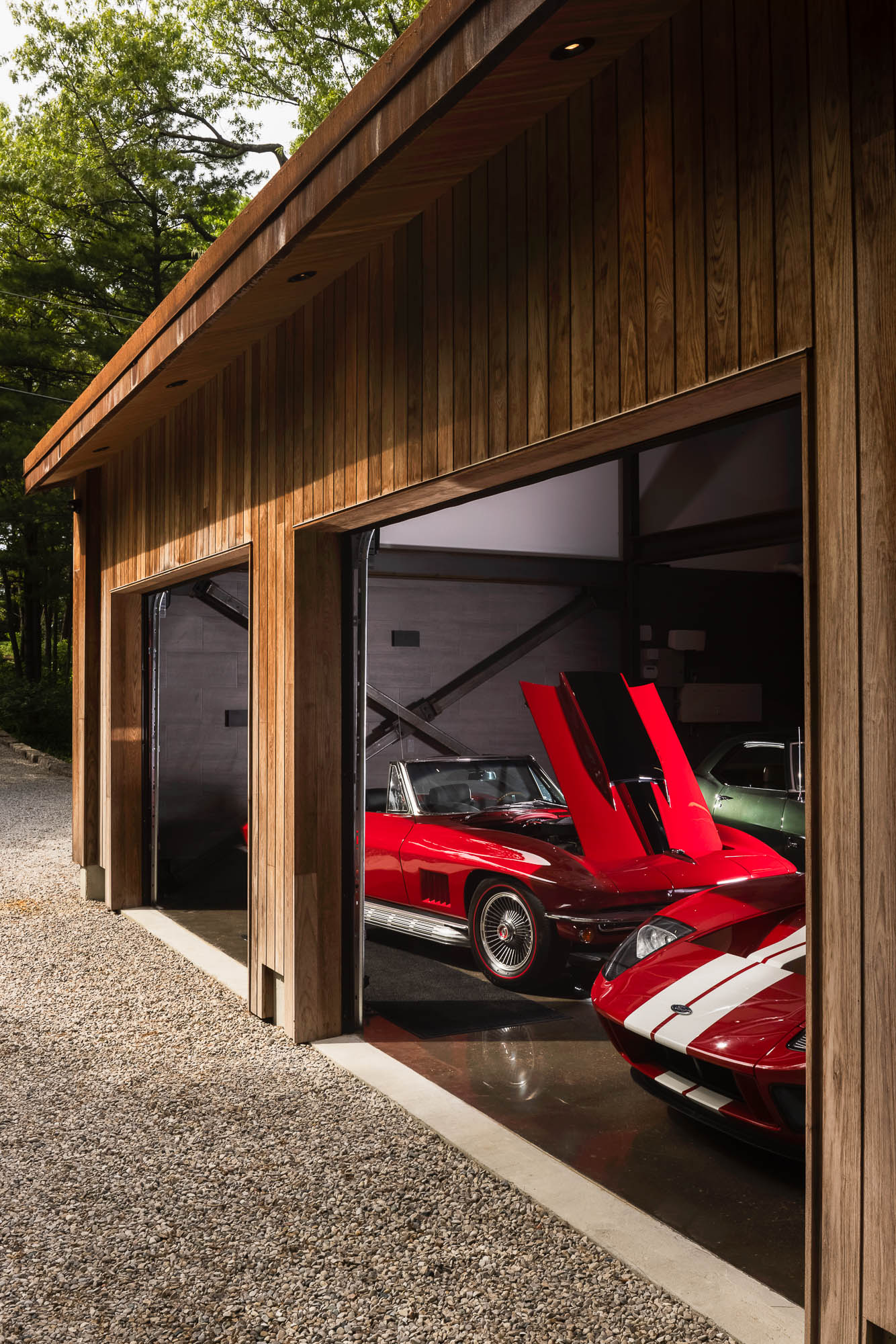 Modern Car Barn Exterior Detail and Classic Collection Exterior shot of open garage doors revealing a red C2 Corvette and Ford GT, framed by vertical wood siding.