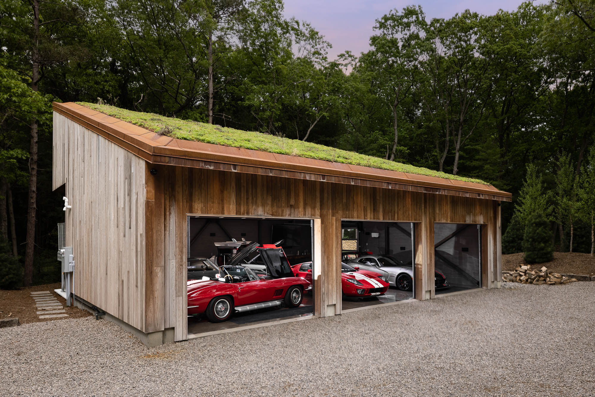 Architectural Overview of Finch Garage Project Profile view of a large wooden garage with a sloping green roof set against a forest backdrop.