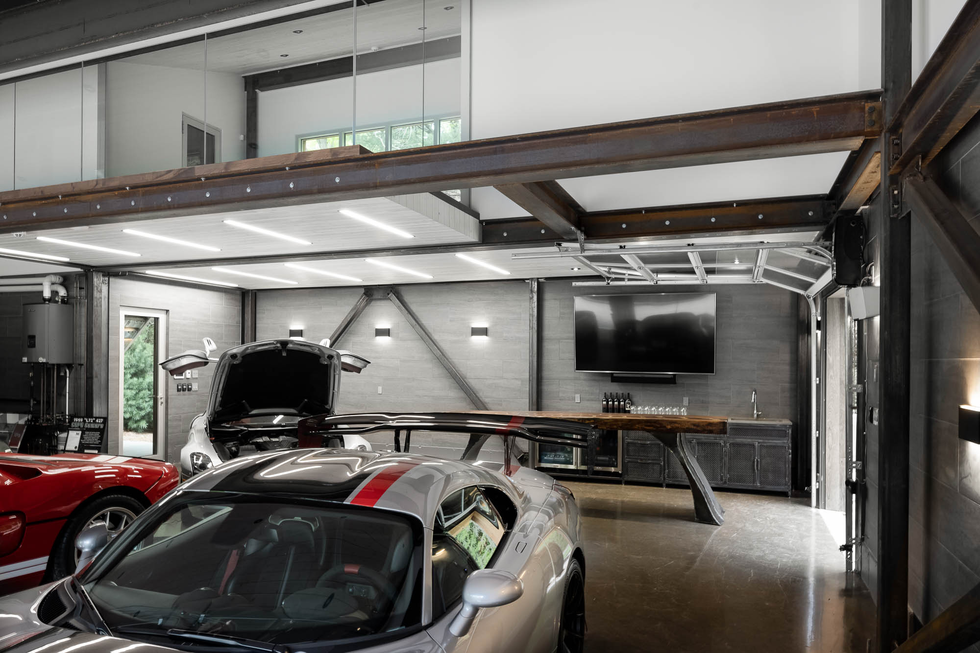Multipurpose Garage Lounge and Mezzanine Interior shot of a garage lounge featuring a live-edge wood bar, mezzanine with glass railings, and industrial steel beams.