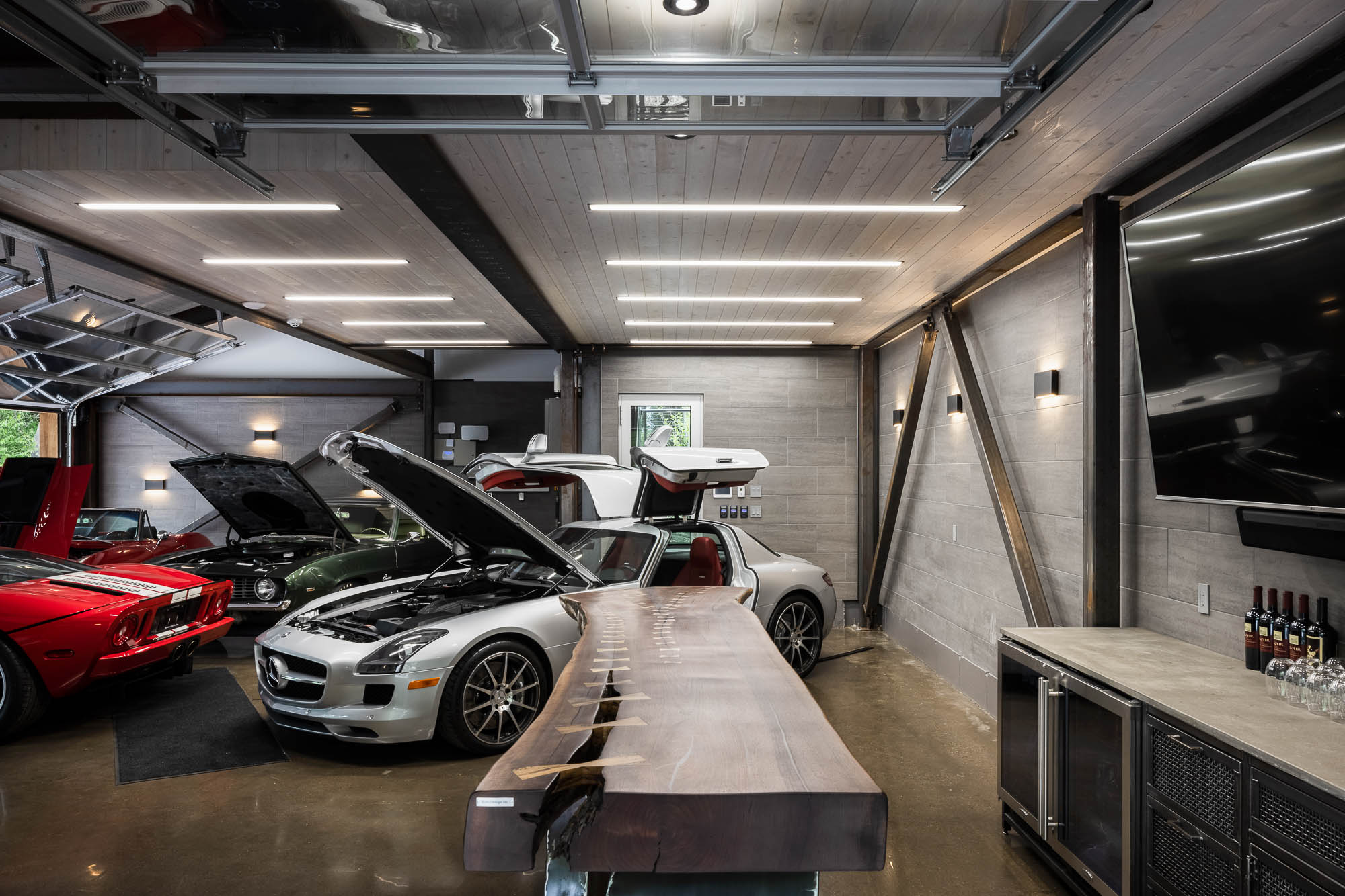 Luxury Garage Interior with Custom Social Space Interior perspective with a live-edge bar in the foreground and a silver Mercedes SLS AMG with open gull-wing doors.