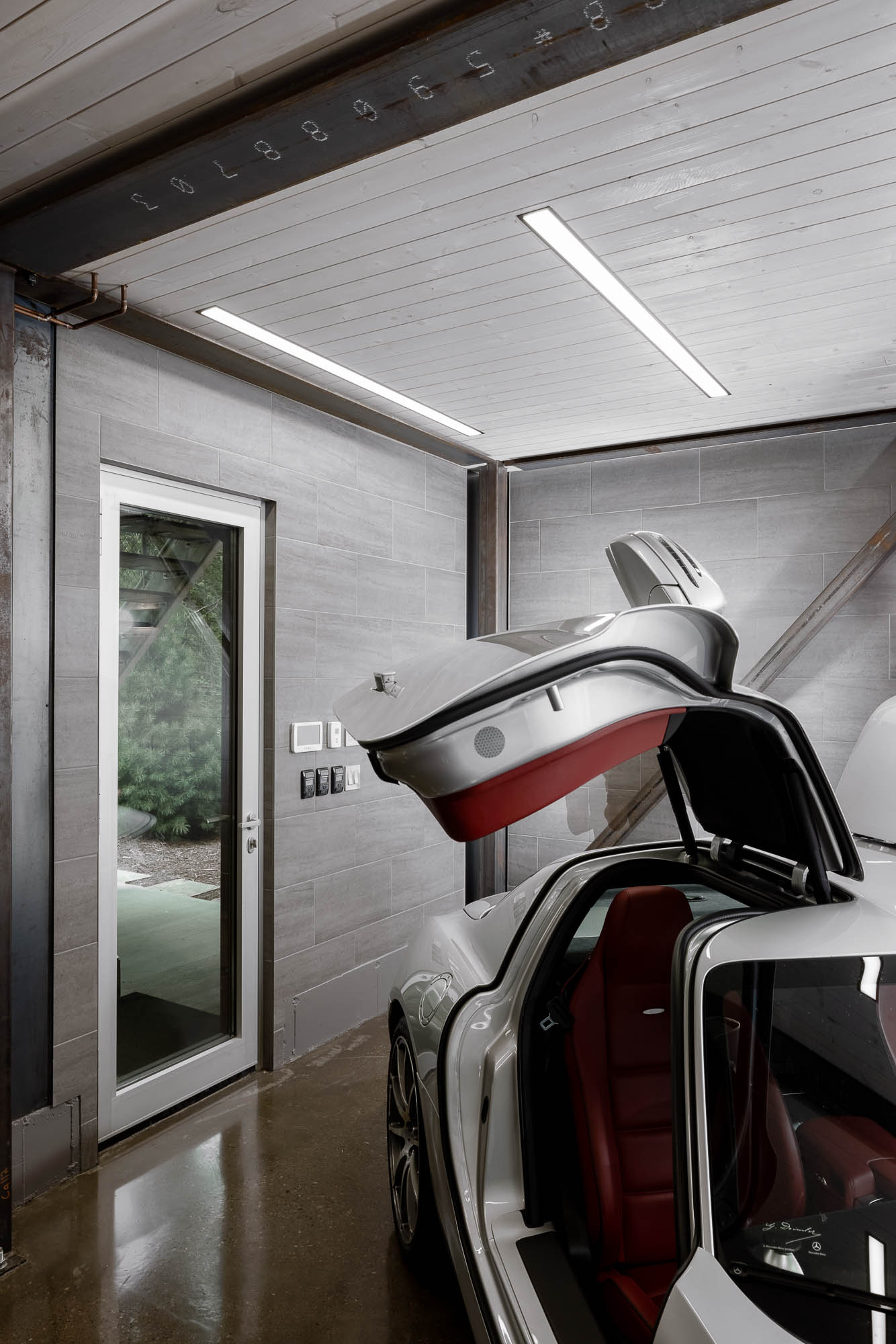 Minimalist Interior Detail of Modern Garage Close-up of an interior white door, grey tile walls, and the gull-wing door of a silver luxury car.