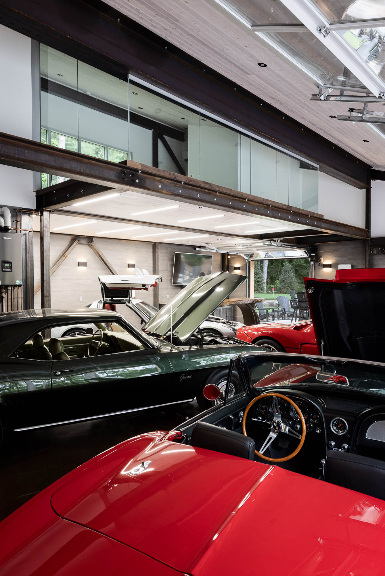 Modern Luxury Garage with Classic Car Collection A high-end modern garage interior featuring a collection of classic cars, including a green Chevrolet Camaro and red Corvette, under a mezzanine level with glass railings.