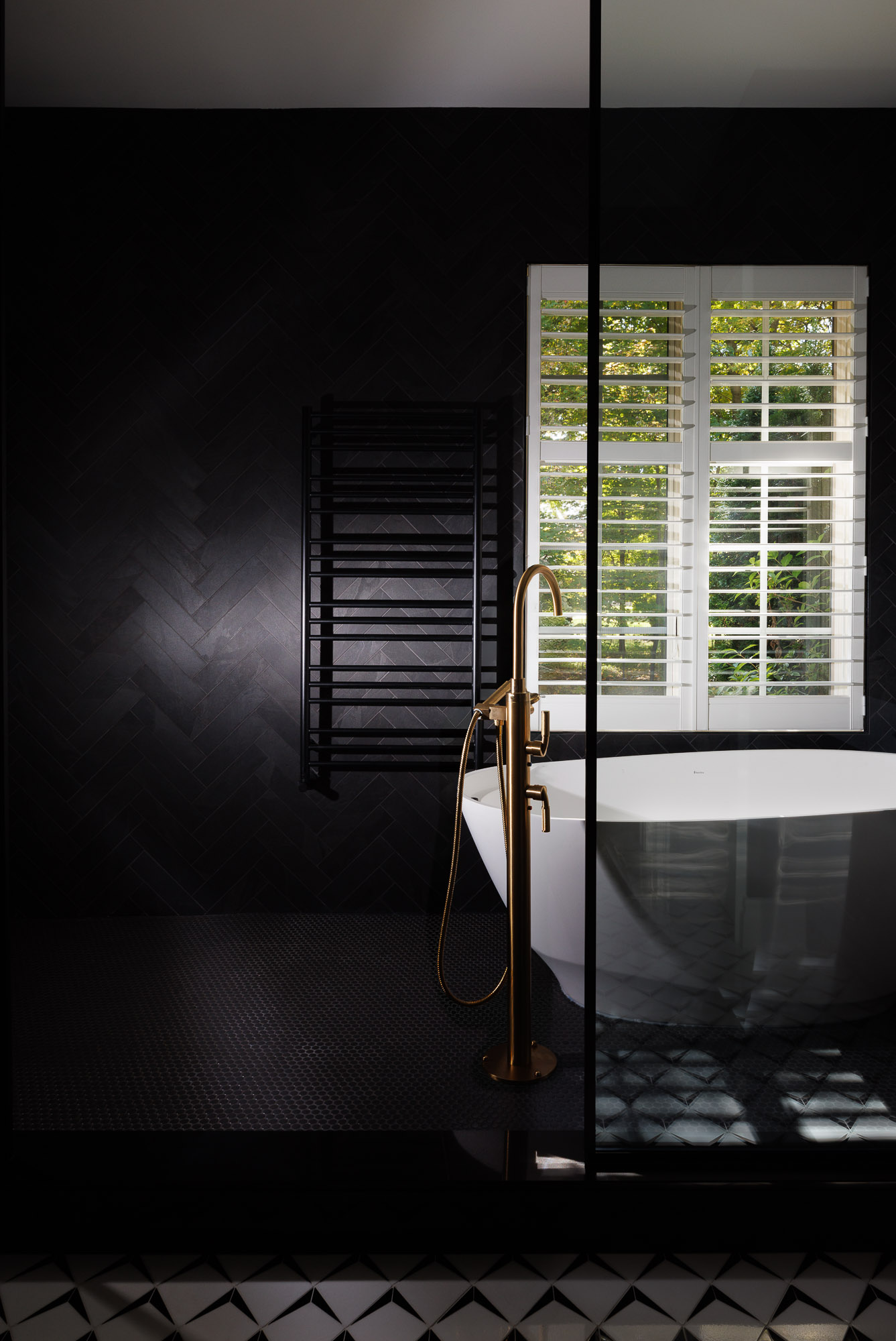 black-herringbone-tile-gold-shower-master-suite Modern master bathroom featuring black herringbone wall tiles, brushed gold shower fixtures, and black penny floor tiles in a villa.