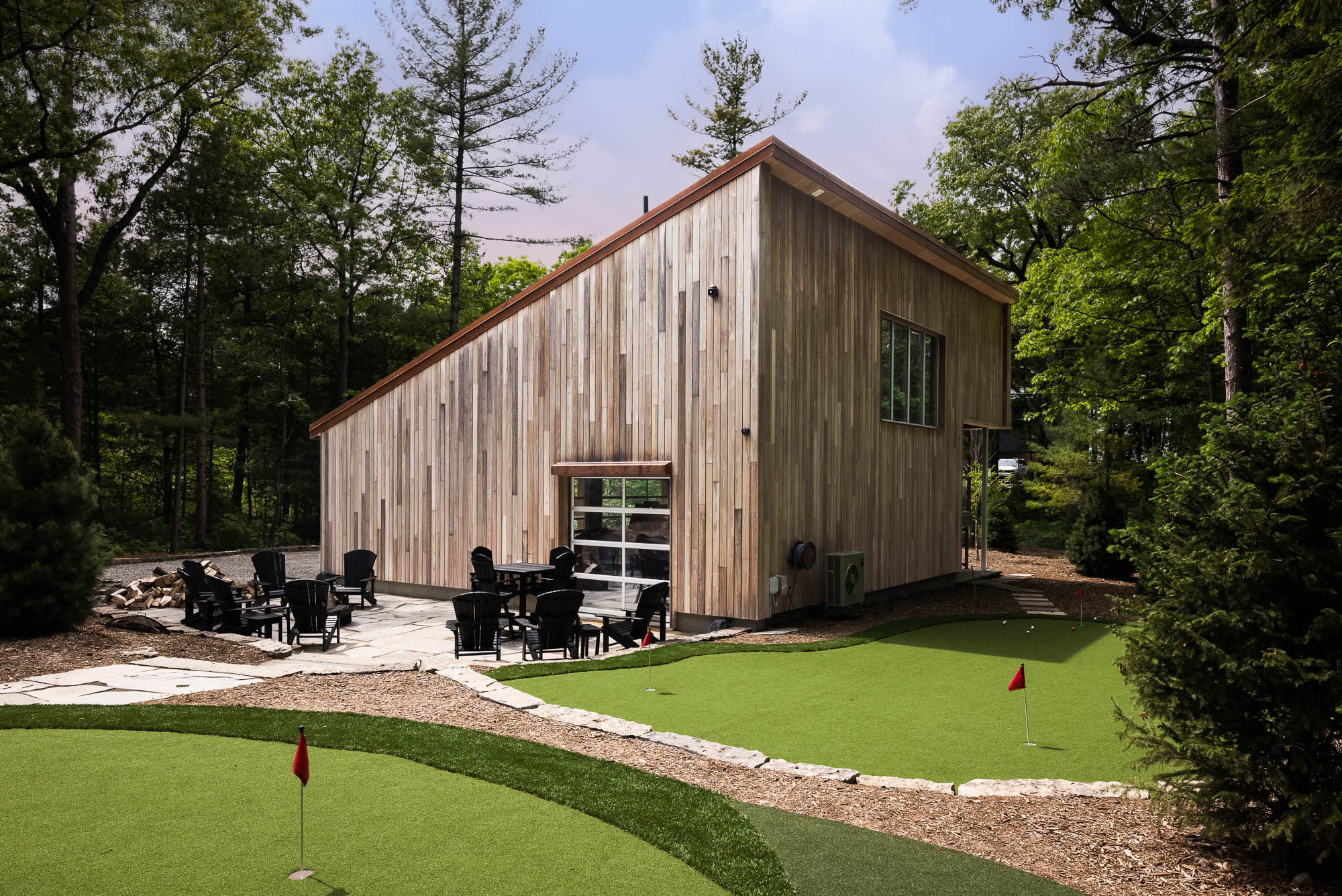 Luxury Stone Patio and Outdoor Seating Stone patio with black Adirondack chairs and a modern glass garage door leading to a wood-clad studio.