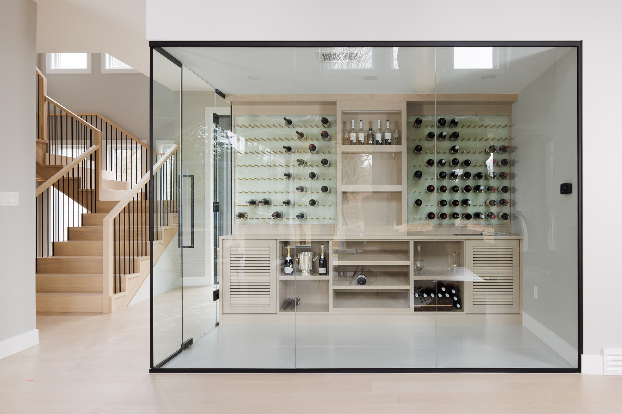 A wide shot of a temperature-controlled glass wine cellar with custom cabinetry and backlit shelving.