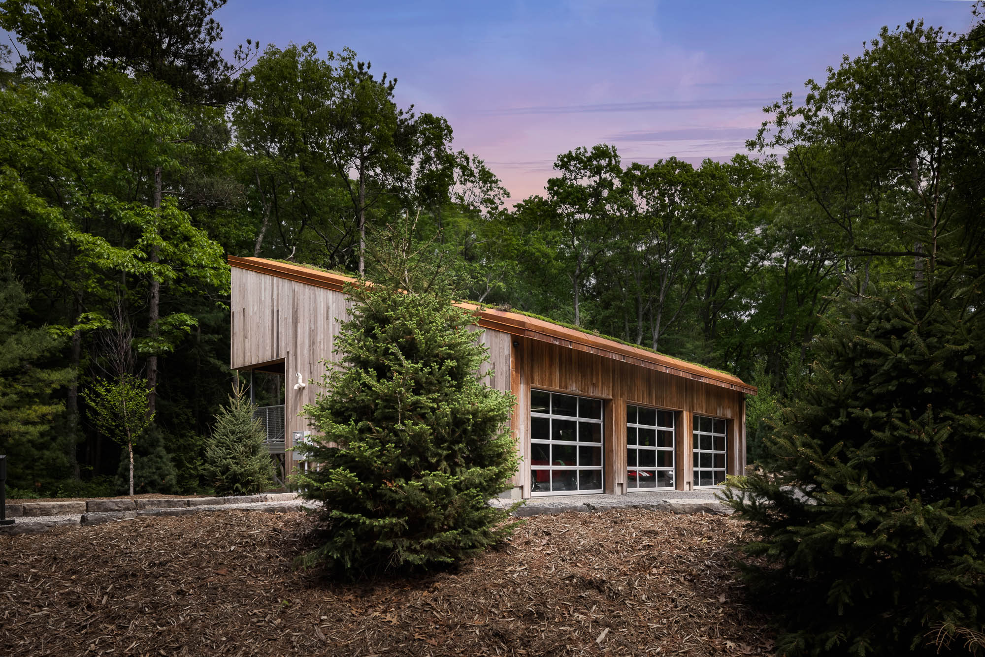 Sustainable Modern Garage Design Wide architectural view of a sloped-roof building with a green roof, framed by evergreen trees and mulch landscaping.