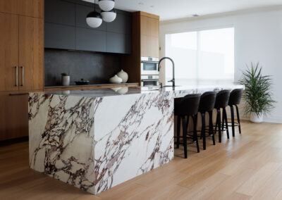 Modern kitchen with a striking white and purple veined marble waterfall island, black bar stools, wood cabinets, and sleek integrated appliances.