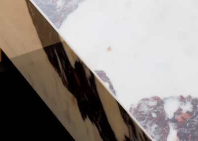 Close-up of two polished marble pieces meeting at a diagonal, one white with grey and reddish-brown veins, the other a beige and dark brown streaked edge.