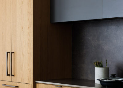 Modern kitchen with light oak wood and dark gray cabinets, dark backsplash, and marble countertop