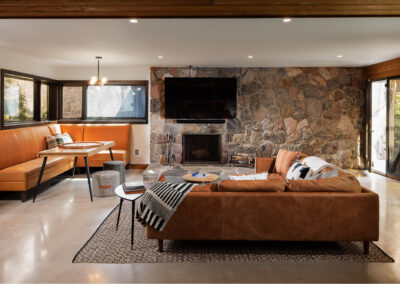 Modern rustic living room with brown leather sofa, stone fireplace, mounted TV, and orange banquette seating