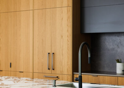 Modern kitchen with full-height light wood cabinets, a luxurious white marble island countertop featuring brown veining, and a sleek black gooseneck faucet.