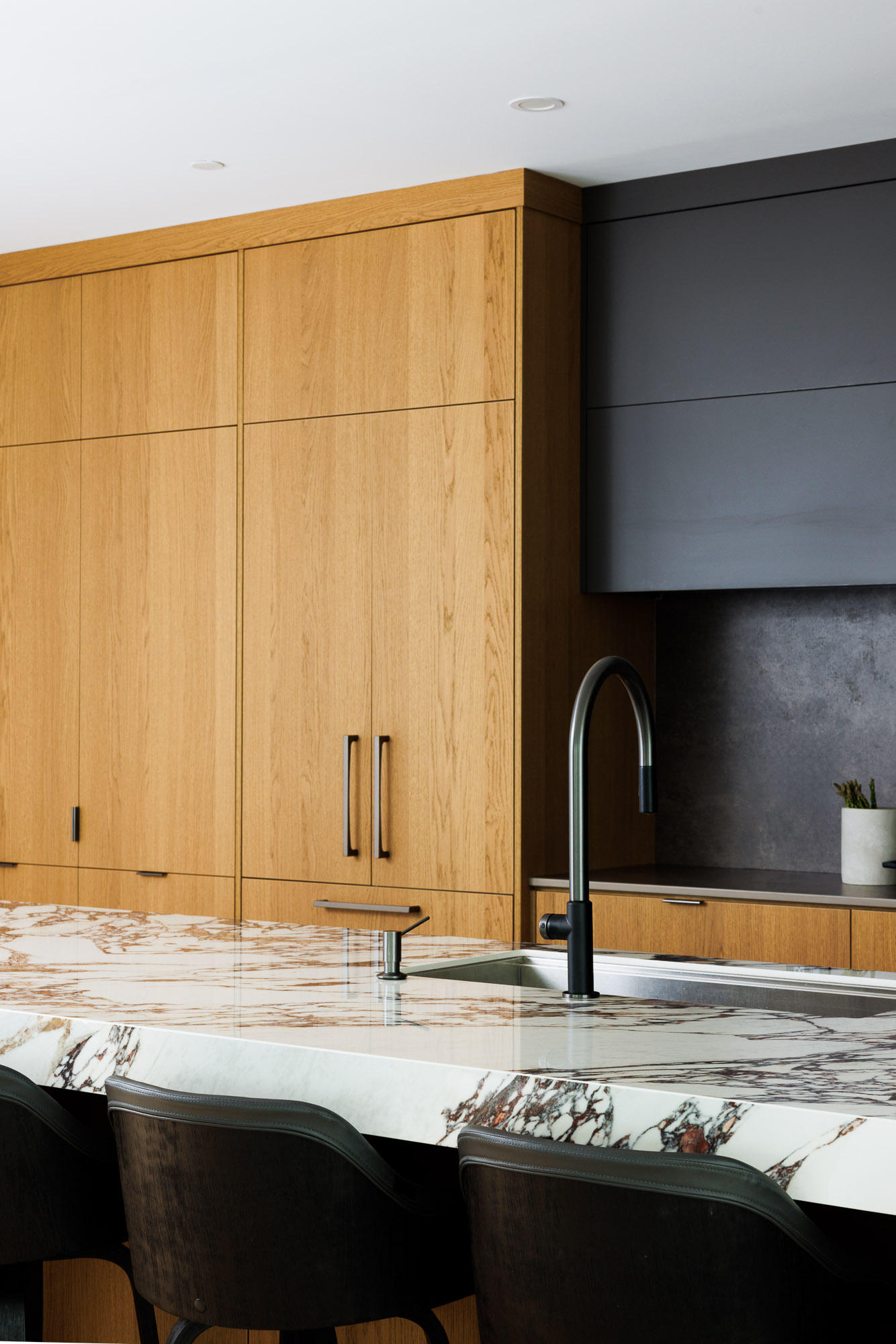 Modern kitchen with full-height light wood cabinets, a luxurious white marble island countertop featuring brown veining, and a sleek black gooseneck faucet.