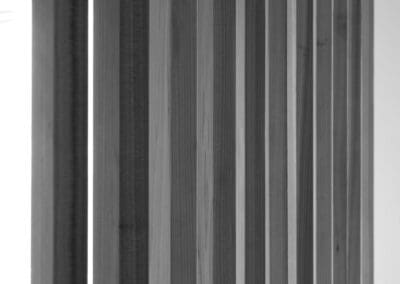 Black and white image of vertical wooden slats, forming a modern room divider or wall panel with natural light from the left.