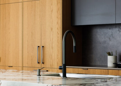 Modern kitchen with natural wood cabinets, dark grey upper cabinets, and a marble island countertop with a black faucet.