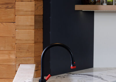 Modern kitchen or bar area with black faucet, white marble countertop, and wooden block wall