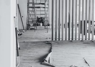 Black and white image of an interior construction site with a shovel in the foreground, scaffolding, and a modern wooden slatted partition.