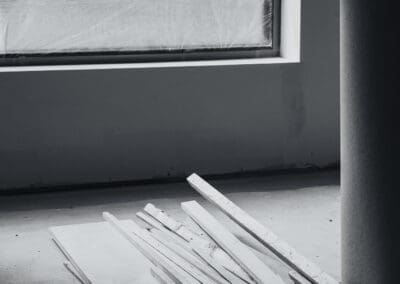 Black and white construction site with wood planks on a concrete floor and a plastic-covered window, showing a renovation in progress.