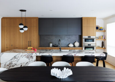 Modern open-plan kitchen with a large white marble island, light wood cabinetry, dark gray upper cabinets, and a dining area.