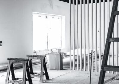 Black and white interior construction scene with saw horses, slat partition, and covered window
