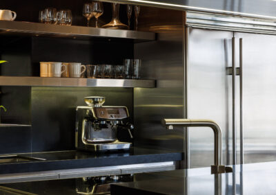 Modern luxury kitchen with espresso machine, sleek stainless steel appliances, black countertops, and a stylish gold faucet.