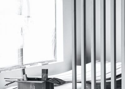 Black and white photo of an interior space under construction, showing a window covered in plastic sheeting with 'DYNAMIC' logos and a modern vertical wooden slat partition.