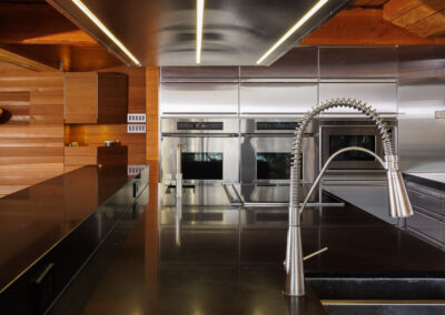 Modern luxury kitchen featuring dark countertops, a professional stainless steel spring faucet, integrated stainless steel appliances, and warm wooden paneling with linear LED lighting.