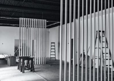 Black and white photo of a modern commercial interior under construction, featuring vertical architectural slat dividers, exposed industrial ceiling, and construction equipment like ladders and sawhorses.