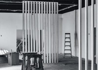 Black and white interior showing construction progress with new wooden slat walls, sawhorses, and a ladder.